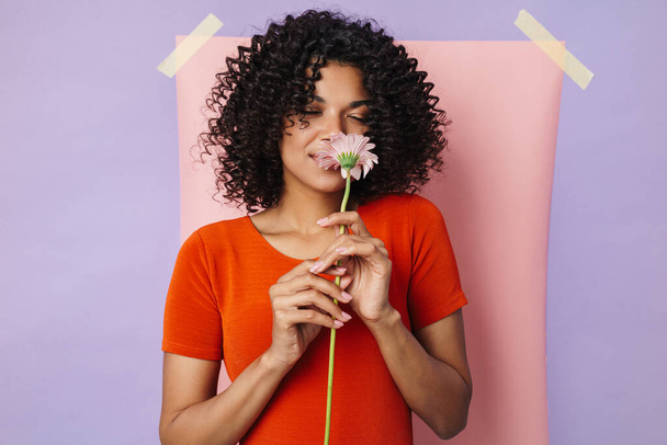 Image of smiling african american woman smelling flower isolated over multicolored background - Φωτογραφία, εικόνα
