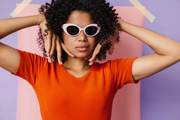 Image of beautiful african american woman in sunglasses looking at camera isolated over multicolored background - Foto, afbeelding