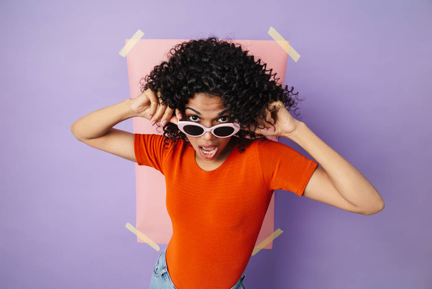 Image of excited african american woman in sunglasses making fun at camera isolated over multicolored wall - Foto, afbeelding