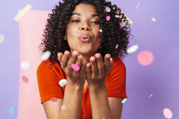 Image of joyful african american woman making fun with confetti isolated over multicolored background - Foto, Imagem