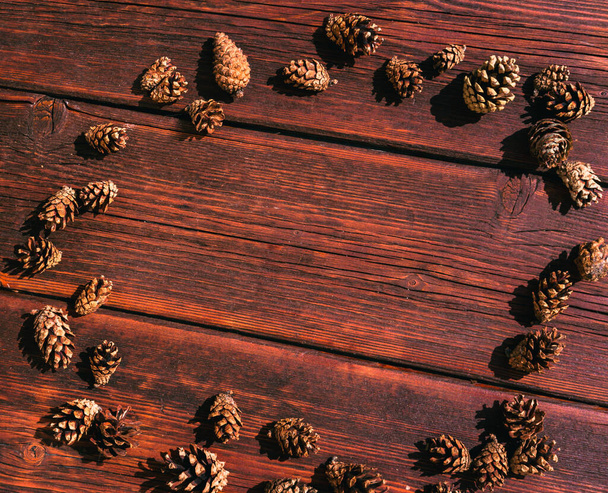 Many small pine cones lie on a mahogany wooden table. Autumn textured background and plenty of space for text and design. - Zdjęcie, obraz