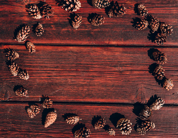 Many small pine cones lie on a mahogany wooden table. Autumn textured background and plenty of space for text and design. - Zdjęcie, obraz
