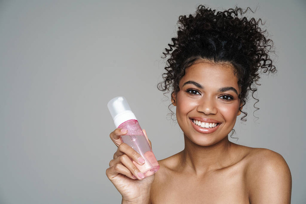 Image of shirtless african american woman smiling while posing with face lotion isolated over grey wall - Zdjęcie, obraz