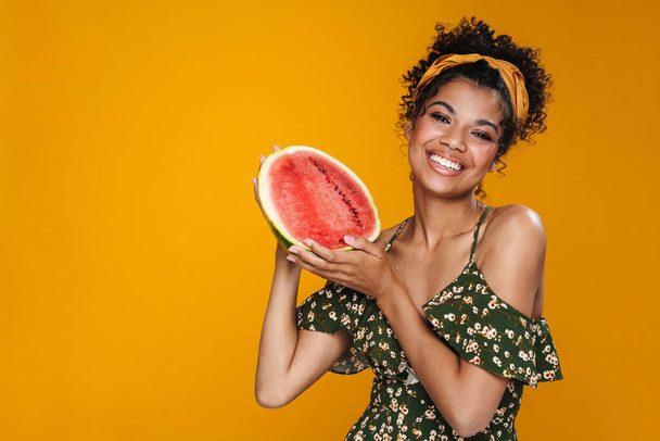 Bild von fröhlichen afrikanisch-amerikanischen Frau lächelt, während posiert Wassermelone isoliert über gelbe Wand - Foto, Bild