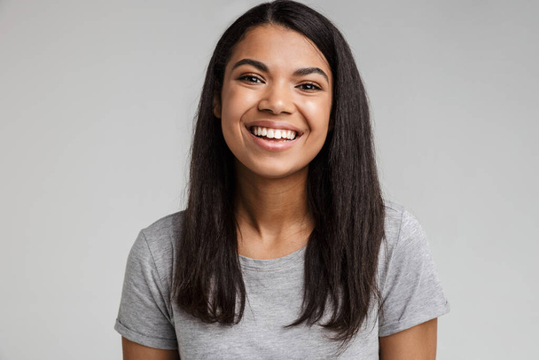 Portrait of a happy smiling young african woman with long dark hair wearing casual clothes standing isolated over gray background - Photo, Image