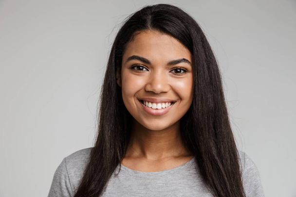 Portrait of a happy smiling young african woman with long dark hair wearing casual clothes standing isolated over gray background - Foto, immagini