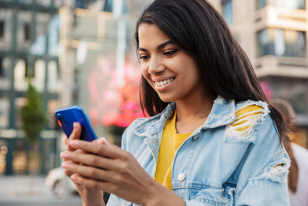 Young smiling casual african woman using mobile phone on a street - Photo, Image