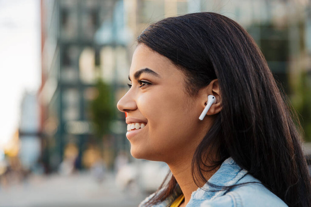 Beautiful african woman listening to music with wireless earphones in a city street - Foto, Bild