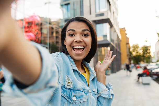 Image of joyful african american woman smiling and taking selfie photo while walking at city street - Photo, Image