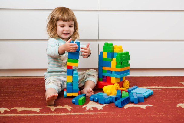 Little child girl playing with lots of colorful plastic blocks constructor sitting on a floor indoor. - Fotó, kép