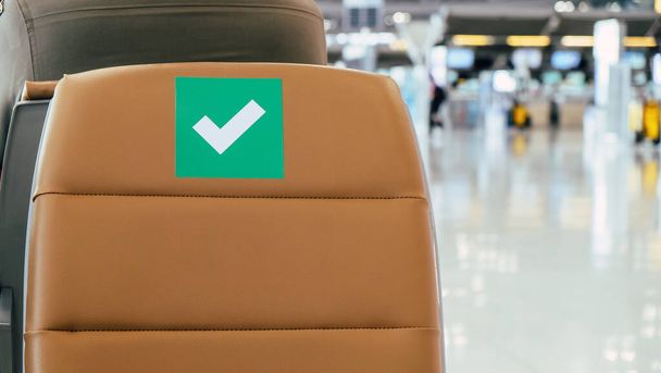 社会的距離、新しいコロナウイルスの拡散を防ぐための社会的距離プロトコルに関するシンボルがマークされた空港の出発エリアの空の椅子の行、タイのCOVID-19 - 写真・画像