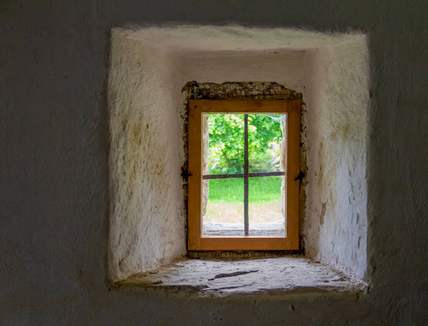 Kalın bir duvarın içindeki tarihi bir pencereden görünen güneşli manzara. - Fotoğraf, Görsel