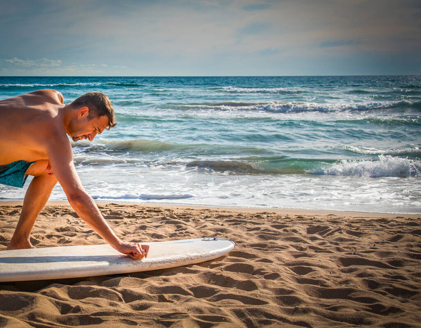 Uomo ceretta una tavola da surf sulla sabbia prima della sessione di surf - Foto, immagini