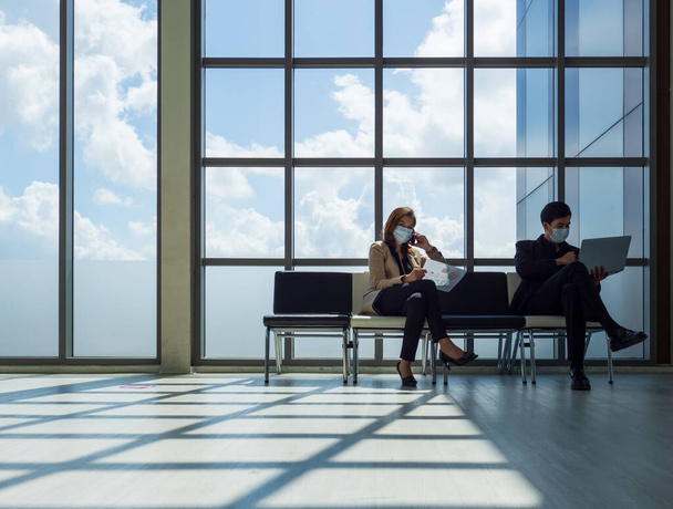 Бизнесмен и деловая женщина в защитной маске сидят на расстоянии между креслами для защиты во время пандемии коронавируса, Ковид-19. - Фото, изображение