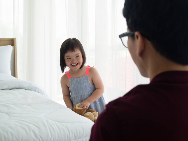Nettes kleines Mädchen mit Down-Syndrom, das mit Vater im Schlafzimmer Verstecken spielt. Asiatische Familie mit besonderen Bedürfnissen. - Foto, Bild