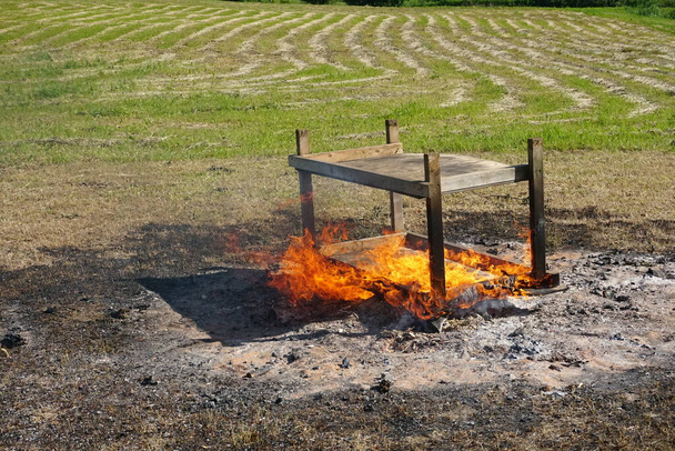 Une vieille table en bois brûle près du feu dans la prairie pendant l'été. - Photo, image