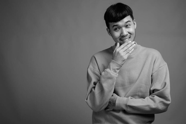 Studio shot of young Asian man wearing sweater against gray background in black and white - Фото, изображение