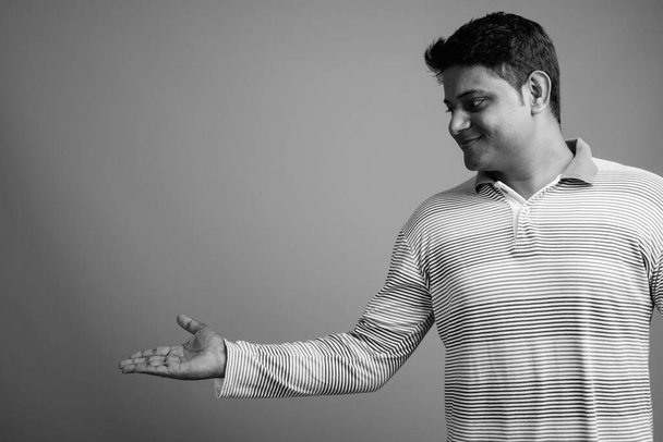 Estúdio tiro de jovem indiano vestindo camisa pólo listrado manga longa contra fundo cinza em preto e branco - Foto, Imagem