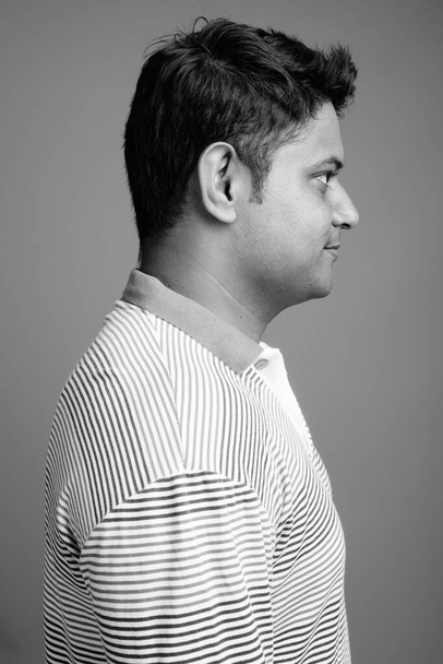 Estudio de un joven indio con camisa de polo de manga larga a rayas sobre fondo gris en blanco y negro - Foto, Imagen