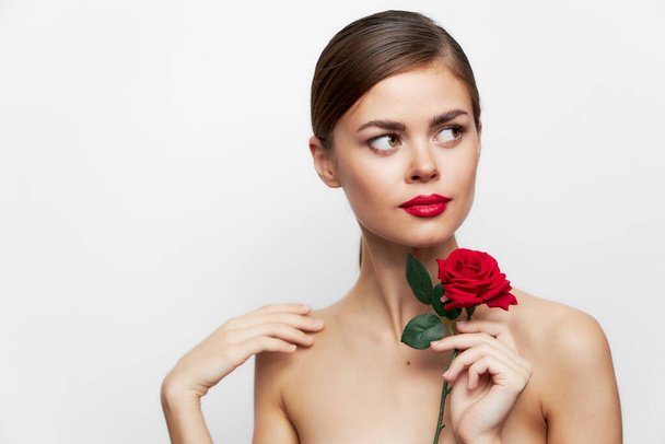 Vrouw met blote schouders kijkt weg met een roos in zijn handen - Foto, afbeelding