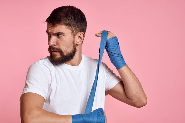 Sporty man in a white T-shirt boxing bandages on the hands of a workout lifestyle pink background - Foto, Imagen