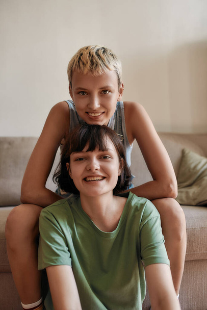 Portrait of young women smiling at camera while cuddling, relaxing at home. Lesbian couple spending time together indoors - Foto, Imagen