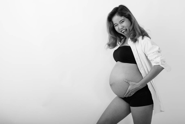 Stúdió lövés fiatal terhes gyönyörű ázsiai nő ellen fehér háttér fekete-fehér - Fotó, kép