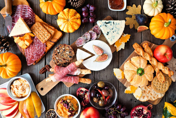 Autumn theme charcuterie table scene against a dark wood background. Variety of cheese and meat appetizers. Overhead view. - Photo, Image