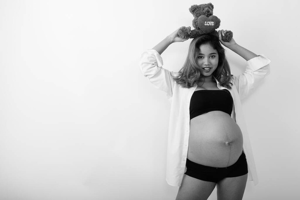 Studioaufnahme einer jungen schwangeren schönen Asiatin vor weißem Hintergrund in schwarz-weiß - Foto, Bild