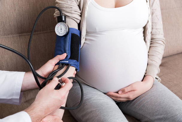 Young doctor is checking blood pressure of pregnant woman at home. High pressure problem during pregnancy concept. - Foto, Imagen