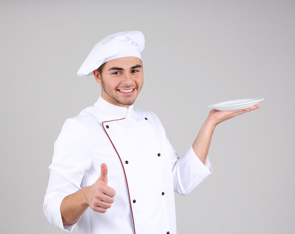Professional chef in white uniform and hat, on gray background - Fotoğraf, Görsel