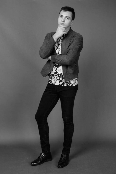 Студийный снимок молодого красивого мужчины в стильной одежде на сером фоне в черно-белом - Фото, изображение