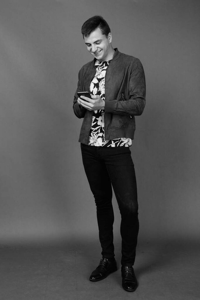 Studioaufnahme eines jungen gutaussehenden Mannes in stilvoller Kleidung vor grauem Hintergrund in schwarz-weiß - Foto, Bild