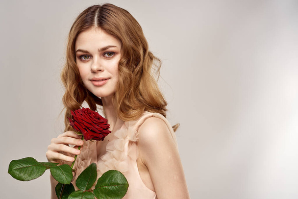 Charming woman with a red rose in her hands on a light background portrait close-up cropped view - Фото, изображение