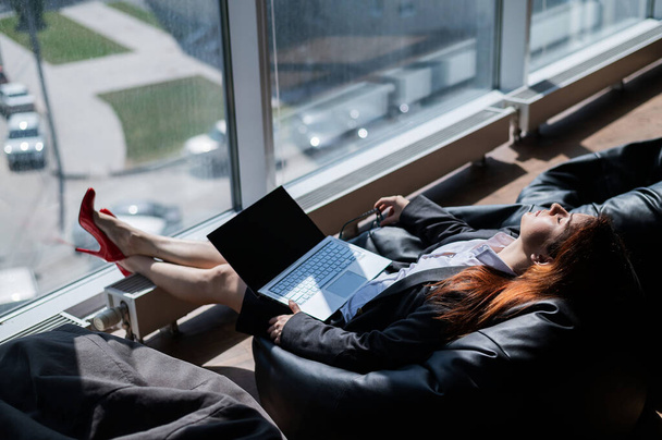 Caucasian woman fell asleep while sitting on bean bag and working on laptop in modern office - Foto, Imagem