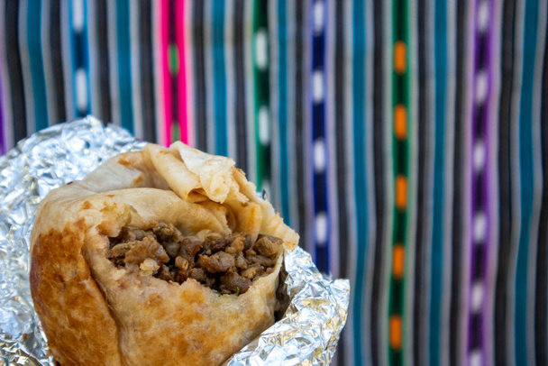 Primer plano de un Burrito Carne Asada con un bocado sacado de él. Burrito está envuelto en papel de aluminio. - Foto, imagen