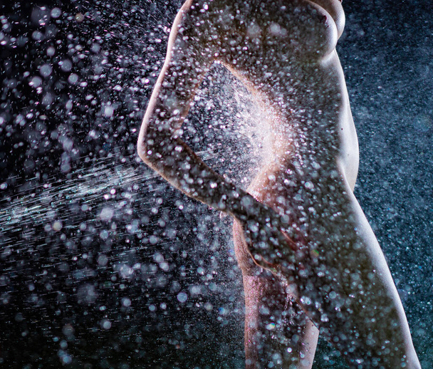 A beautiful European nude woman stands under sprinkler at night - 写真・画像