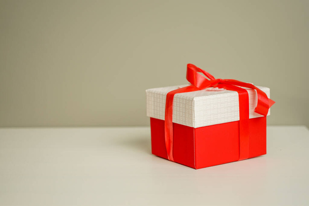 a beautiful red gift box tied with a bright red ribbon lies on the bedside table - Фото, изображение