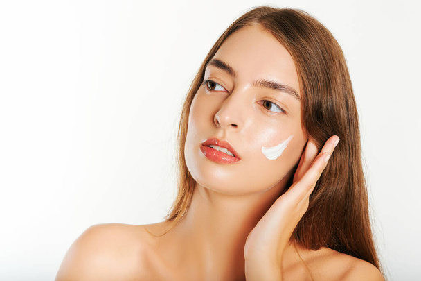 Imagen de cerca de la joven hermosa mujer aplicando crema facial a la cara, fondo blanco - Foto, Imagen