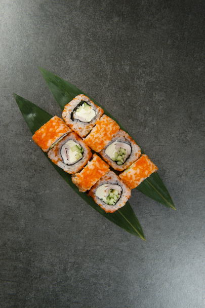 Japanilainen sushi roll savustettua kanaa, kurkkua ja tuorejuustoa tarjoillaan vihreä trooppinen monstera lehtiä antrasiitti tausta. Aasian riisi roll lentävät kala mäti Tobiko - Valokuva, kuva