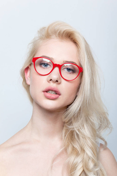 Retrato frontal de uma mulher loira sensual com maquiagem vestindo óculos vermelhos, olhando para a câmera, sobre fundo branco. - Foto, Imagem