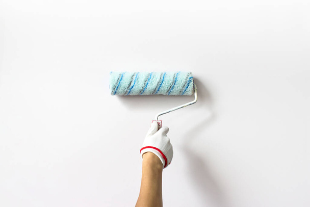 Hand holds paint roller and painting a White wall. Decorator's hand painting wall with roller - Fotoğraf, Görsel