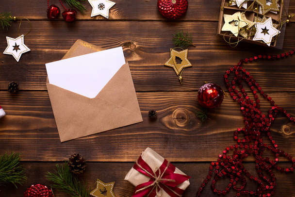 Mail envelope made of craft paper with a white sheet for text on a wooden background with Christmas decor. A letter to Santa Claus, a wish list, a new year's dream, a gift. Flat lay, copy space - Fotografie, Obrázek