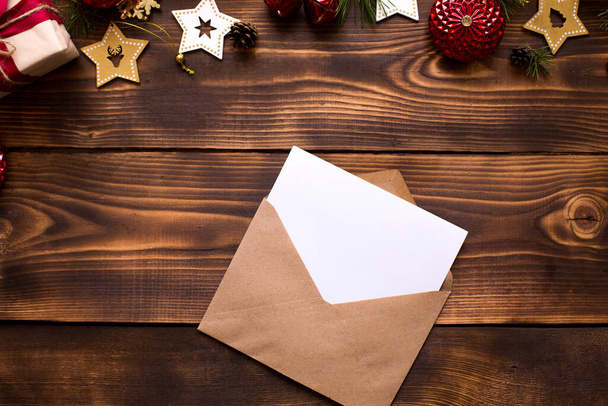 Mail envelope made of craft paper with a white sheet for text on a wooden background with Christmas decor. A letter to Santa Claus, a wish list, a new year's dream, a gift. Flat lay, copy space - Zdjęcie, obraz