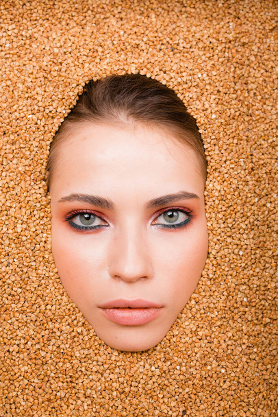 The face of a beautiful girl of a fashion model with glamorous makeup in a scattering of buckwheat. Diet concept. Fashion shooting - Photo, image