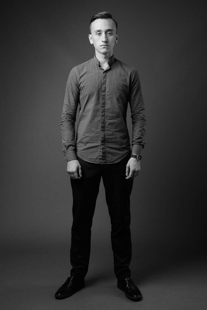 Στούντιο πλάνο του νεαρού όμορφου επιχειρηματία φορώντας κουμπί κάτω πουκάμισο σε γκρι φόντο σε μαύρο και άσπρο - Φωτογραφία, εικόνα