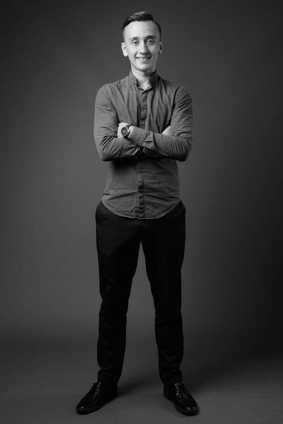 Studioaufnahme eines jungen, gut aussehenden Geschäftsmannes, der Knopfleistenhemd vor grauem Hintergrund in schwarz-weiß trägt - Foto, Bild