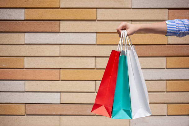 Közelkép a női kéz gazdaság sok színes papír bevásárló táskák a tégla háttér, sablon. - Fotó, kép