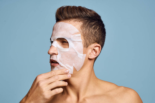 Nude man with white nourishing mask on face on blue background cropped view - Фото, изображение