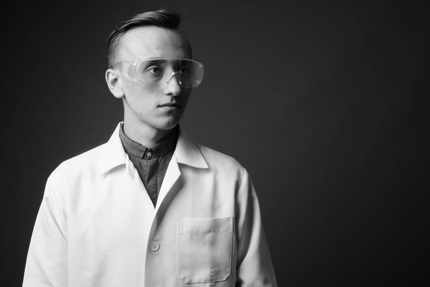 Studio zdjęcie młodego przystojnego lekarza noszącego okulary ochronne na szarym tle w czerni i bieli - Zdjęcie, obraz